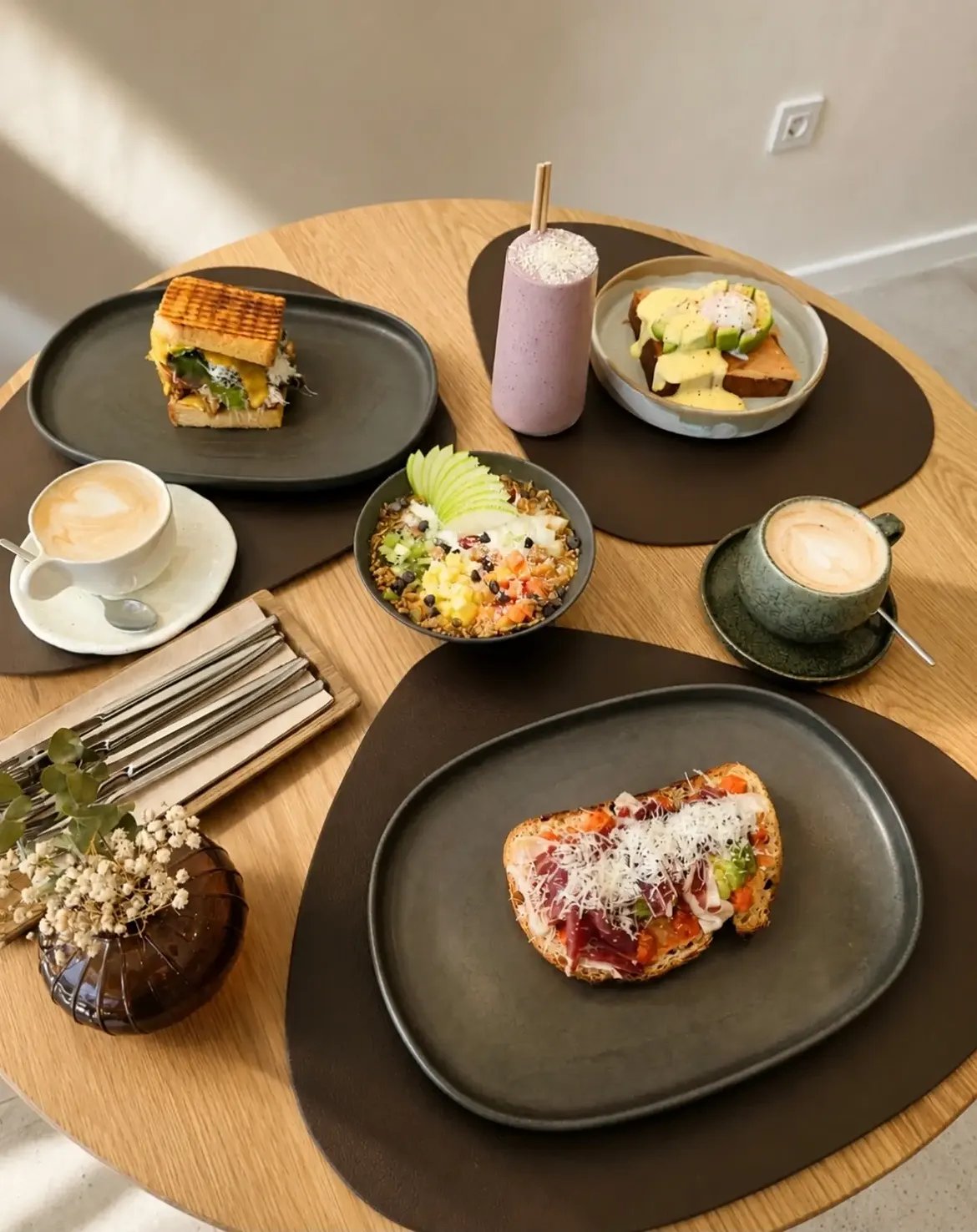 Mesa vista desde arriba con tostas, granola bowl, smoothie morado y cappuccinos