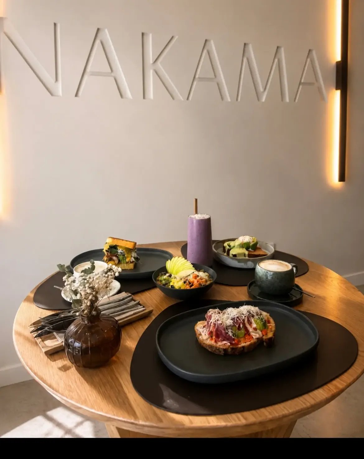 Mesa de Nakama bajo el rótulo de la marca en relieve, con tostas, smoothie y café