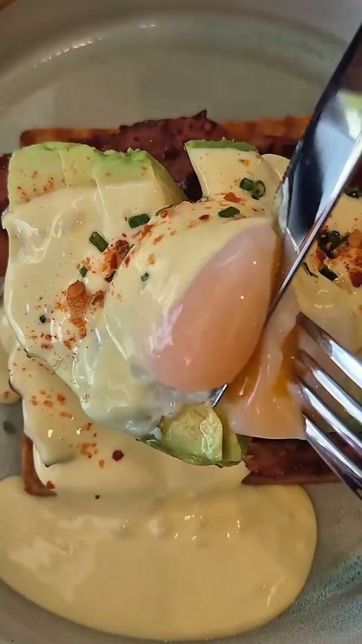 El tenedor corta el huevo pochado y la yema se derrama sobre la tostada