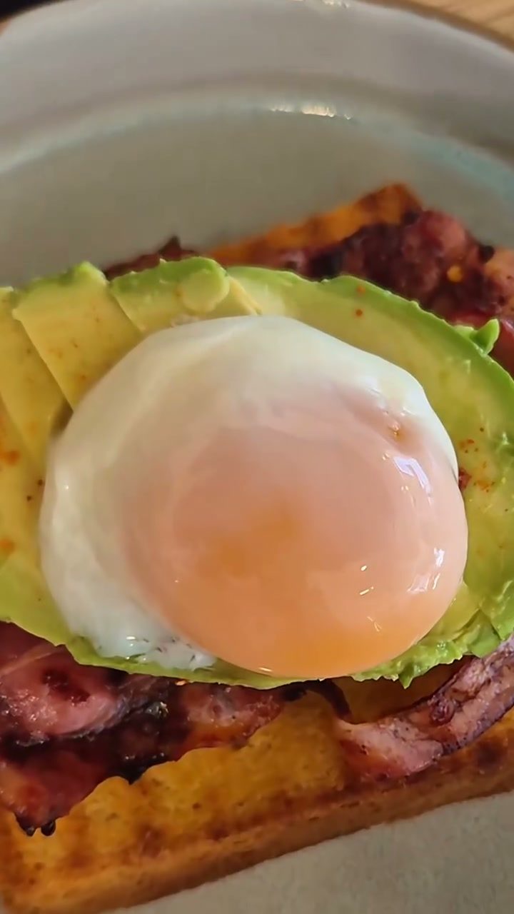 Huevo pochado sobre aguacate y bacon, quieto, a punto de cortarse